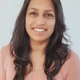 Nicole Jayawickreme, smiling, in a coral top against a white wall