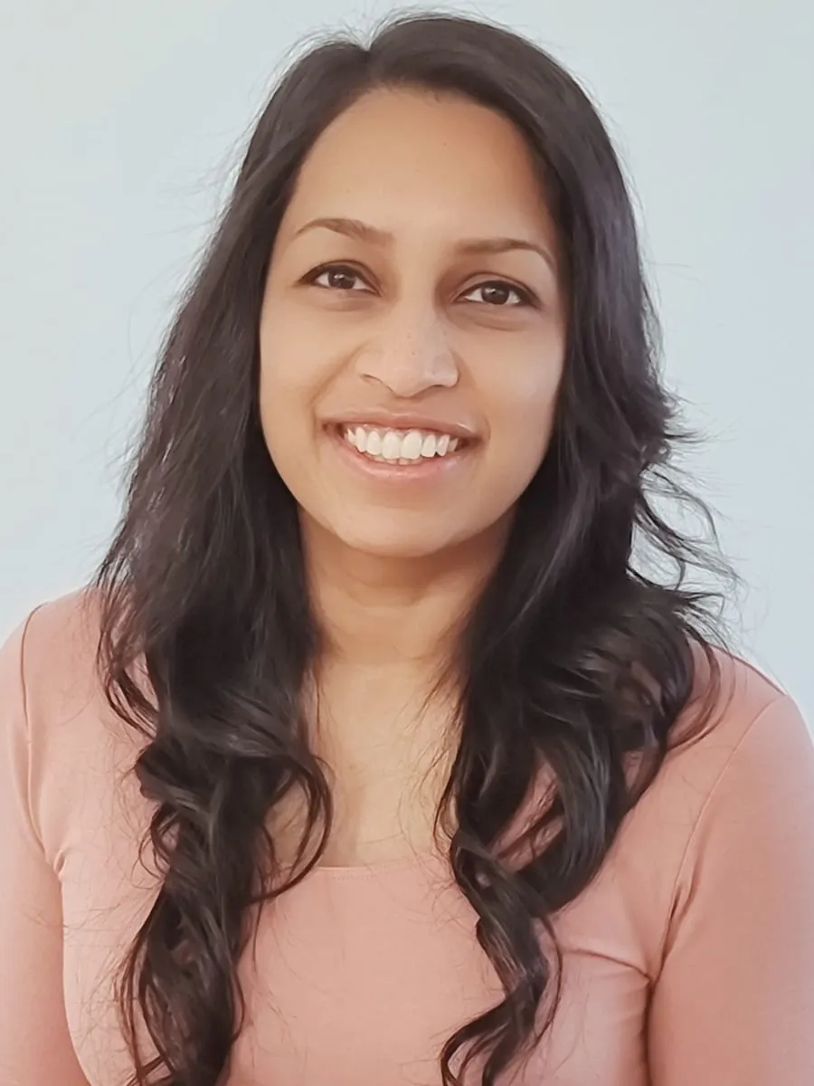 Nicole Jayawickreme, smiling, in a coral top against a white wall