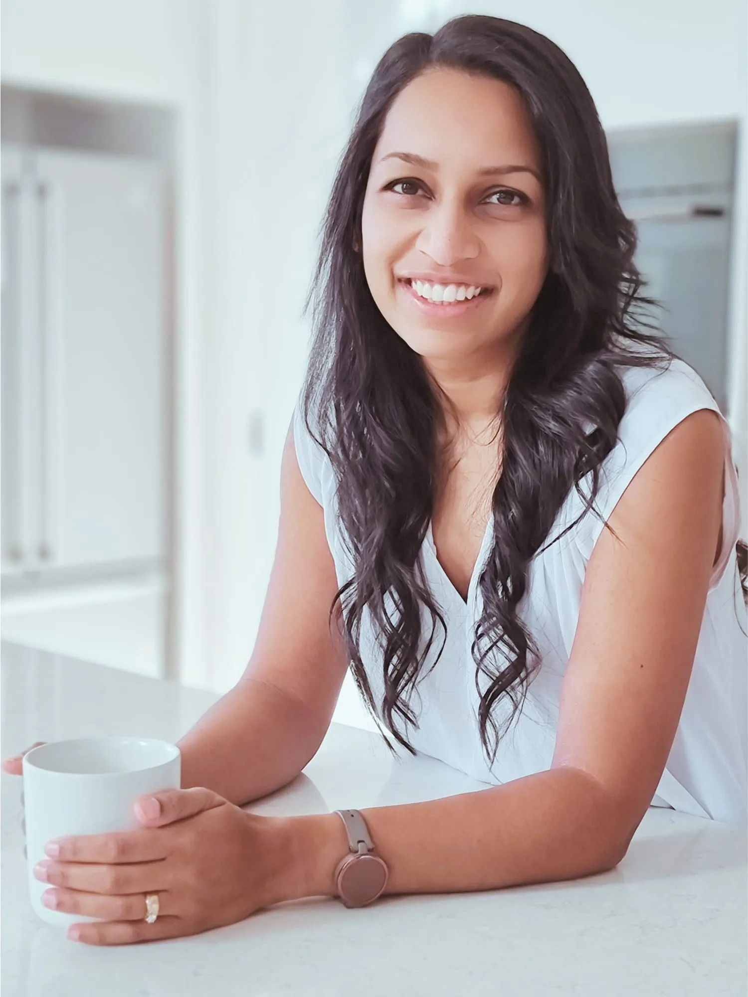 Nicole Jayawickreme leaning on a kitchen bench with a mug, smiling